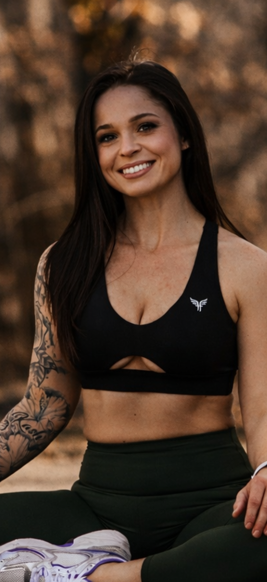 Woman in black sports bra and leggings sitting outdoors with a blurred natural background